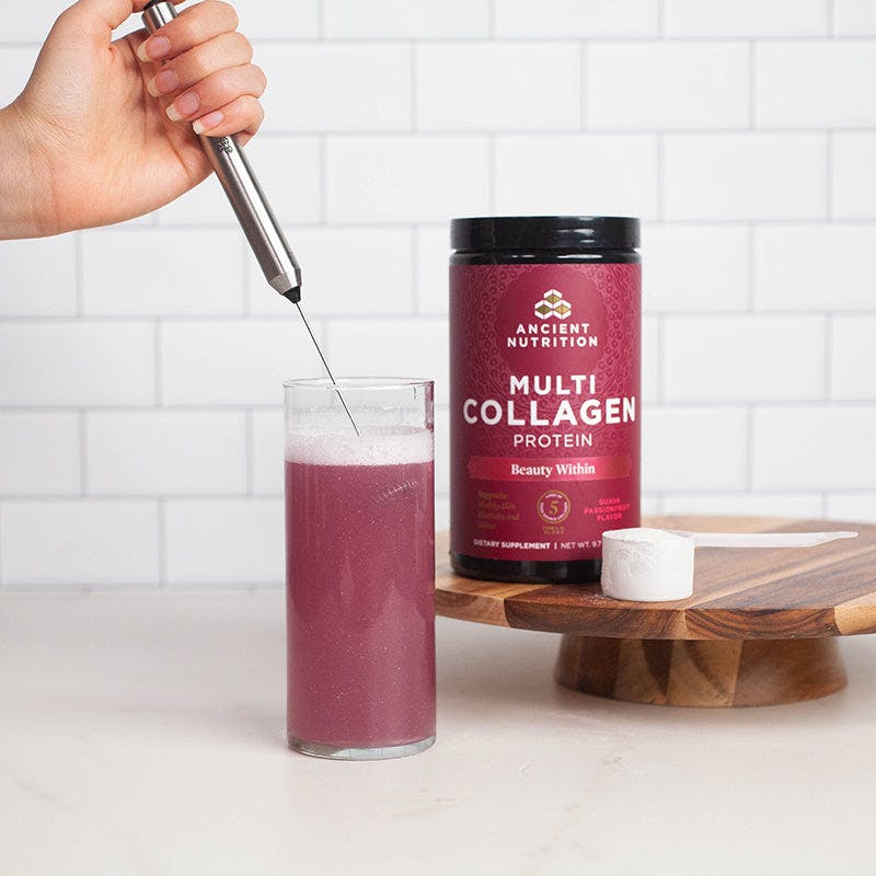 person using frother in a cup next to a bottle of collagen