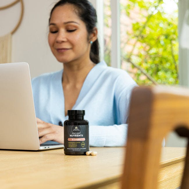 woman working on computer with vitamin b complex on her desk