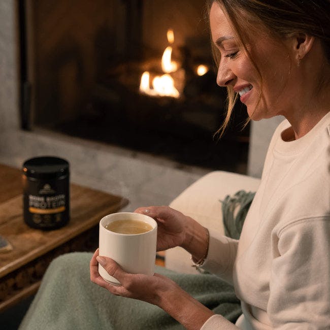 woman by a fire drinking bone broth protein chicken soup 