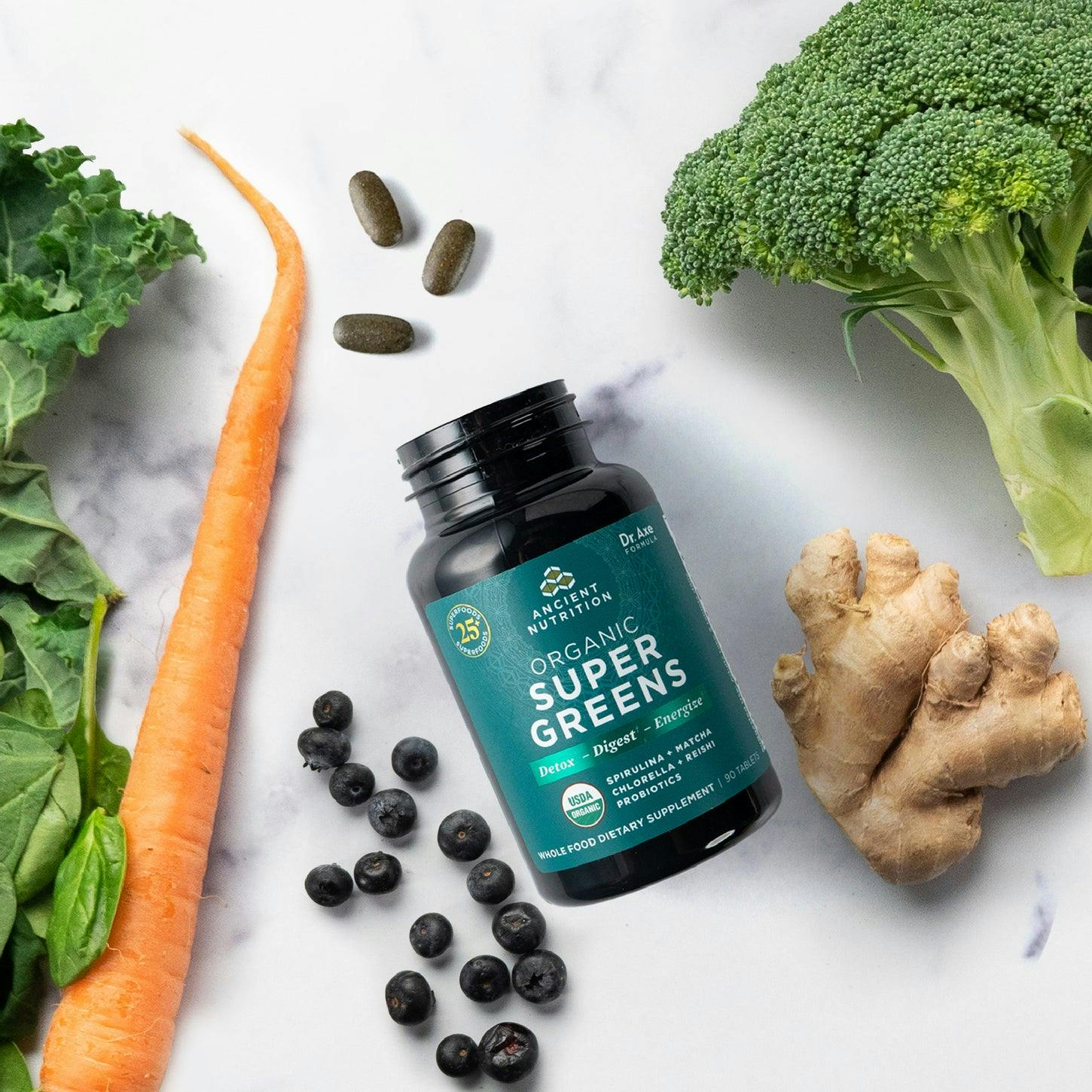 Organic SuperGreens Tablets next to broccoli, carrots and gingerr