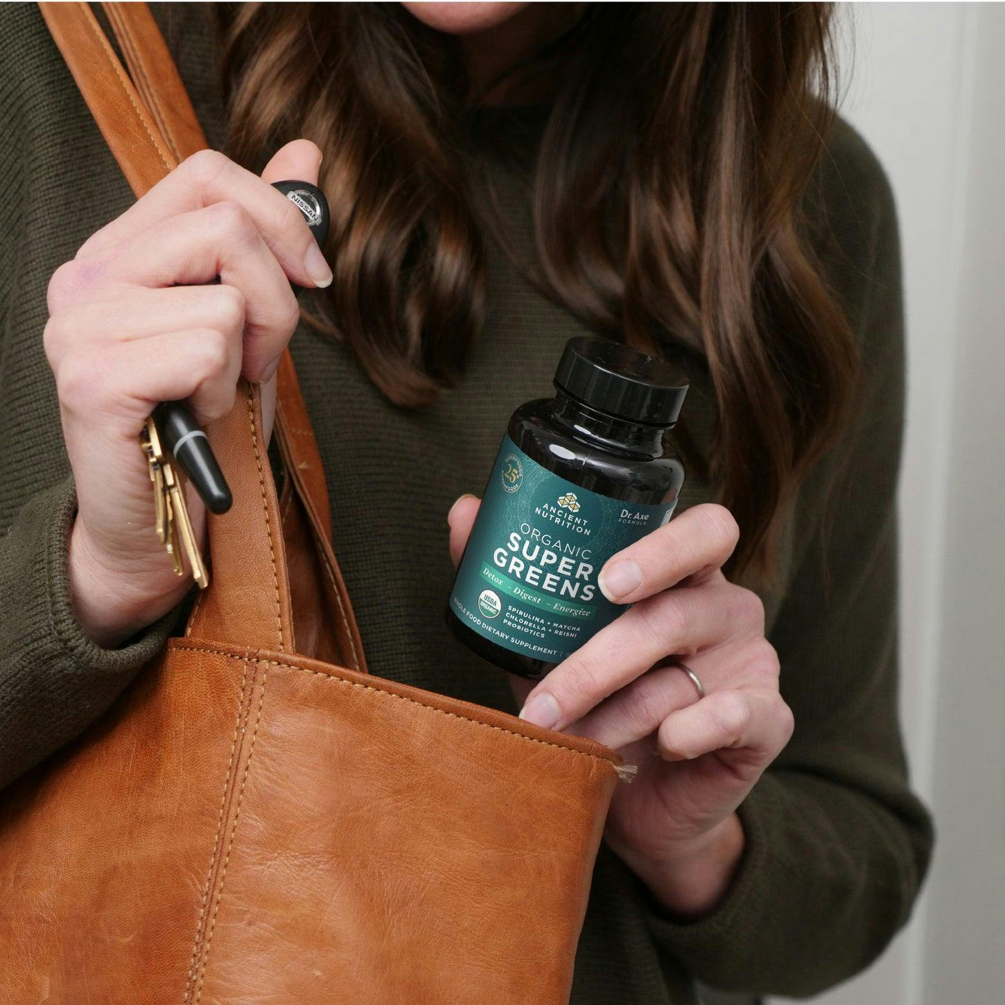woman holding supergreens capsule bottle next to purse