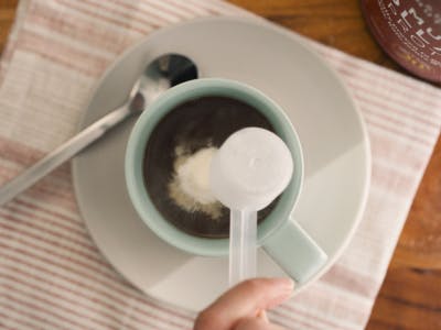 a person adding a scoop of collagen into coffee