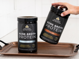 2 containers of Ancient Nutrition bone broth protein with a hand grabbing one