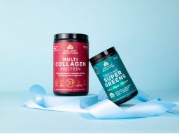 Bottle of multi collagen protein and bottle of organic supergreens on a light blue background