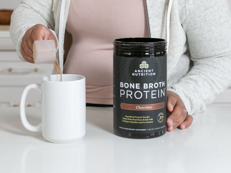 person scooping Bone Broth Protein Chocolate into a cup
