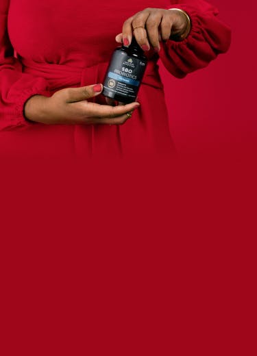 a woman holding a bottle of SBO probiotics Ultimate on a red background